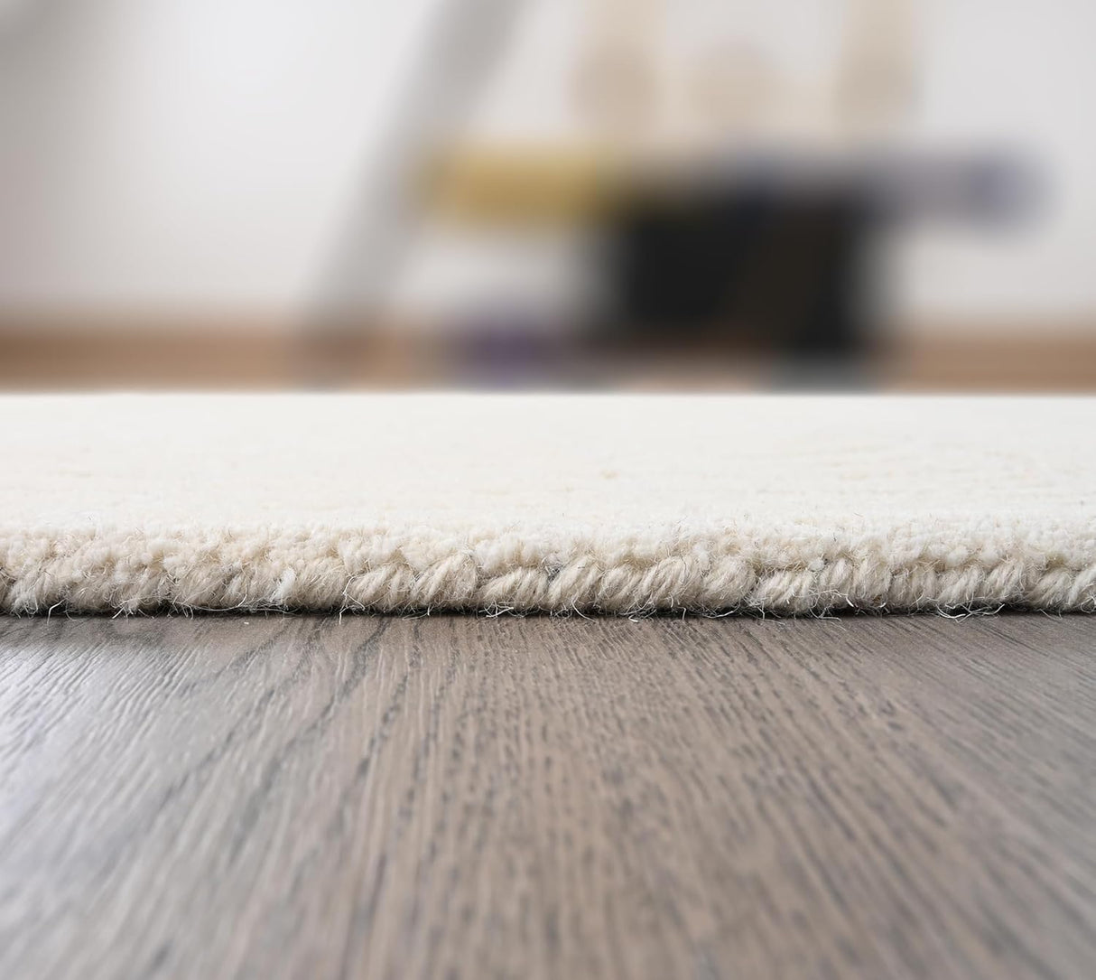 Close-up cream textured rug, woven edge, dark wood floor.
