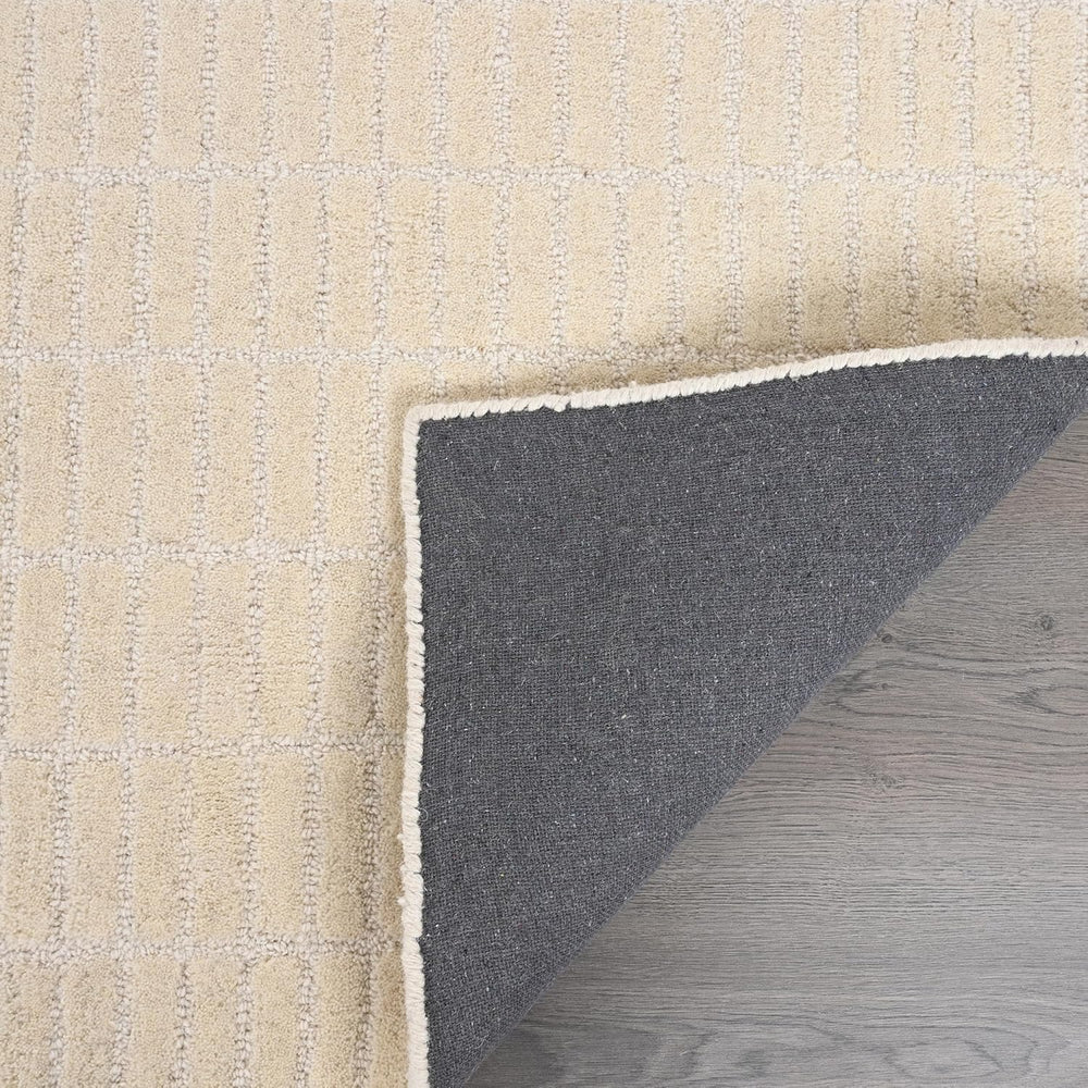 Close-up cream rug, folded corner, grey backing, wood floor.