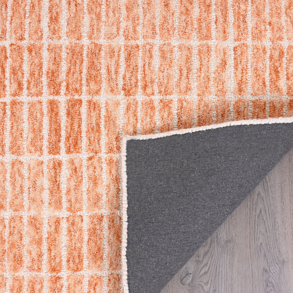 Close-up orange-cream rug with block pattern, folded corner, gray backing.