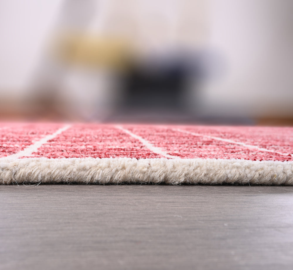 Close-up red rug with white patterns, fringed edge, dark floor.