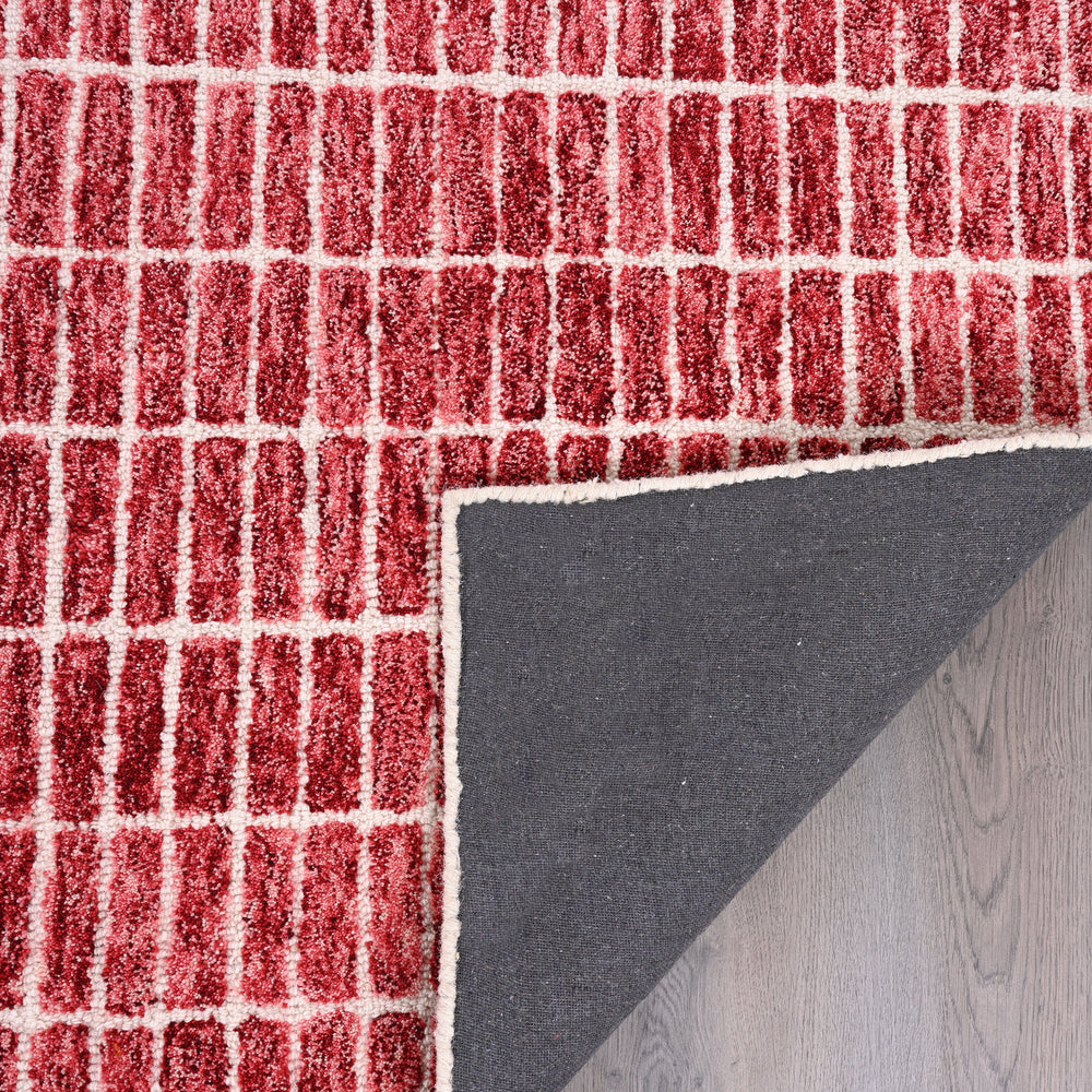 Close-up red-white rug, folded corner, grey underside, wood floor.